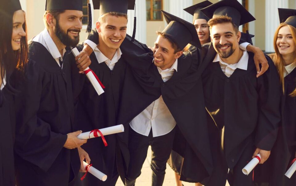 A group of seven students holding their diplomas in graduation regalia and posing together at The Atrium Event Space near Southfield, Michigan (MI)