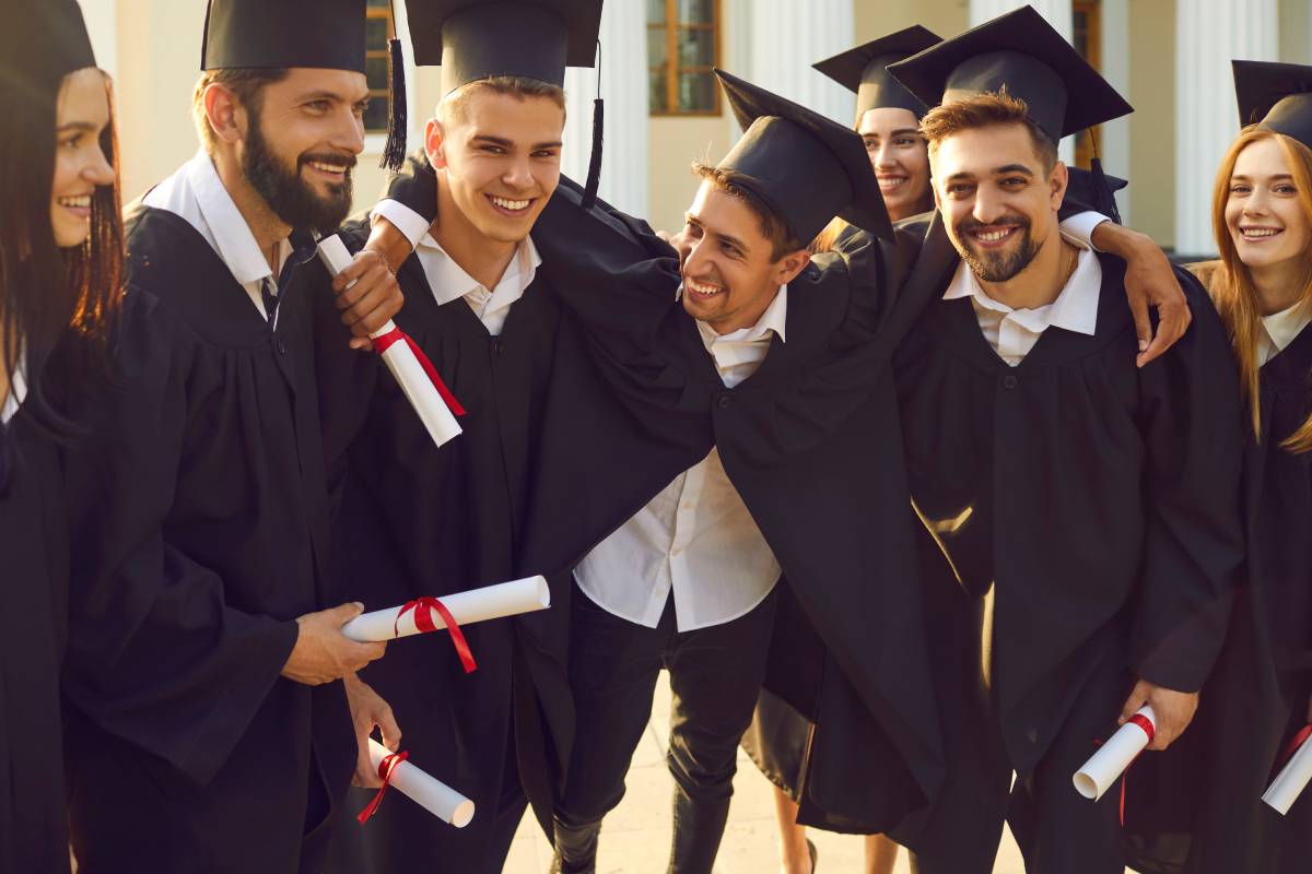 A group of seven students holding their diplomas in graduation regalia and posing together at The Atrium Event Space near Southfield, Michigan (MI)