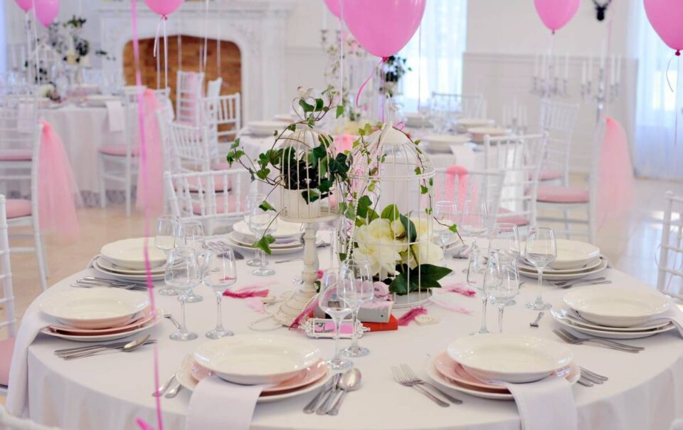 Table in a ballroom with white tablecloths, dinnerware, and glassware with pink balloons for a Sweet 16 at The Atrium Event Space near Southfield, Michigan (MI)