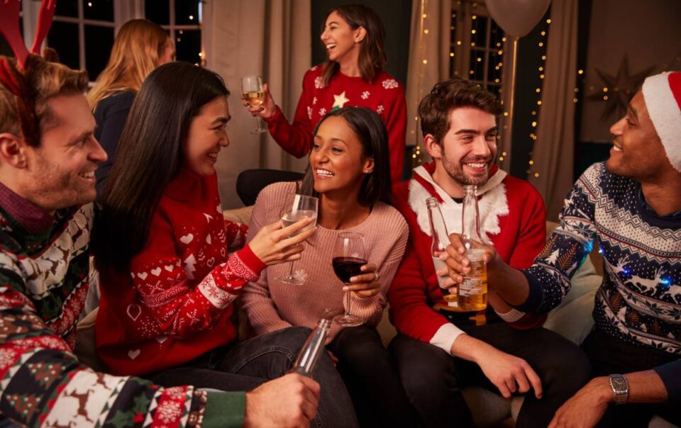 Seven team members wearing holiday sweaters, laughing, and chatting during a corporate holiday party at The Atrium Event Space near Southfield, Michigan (MI)