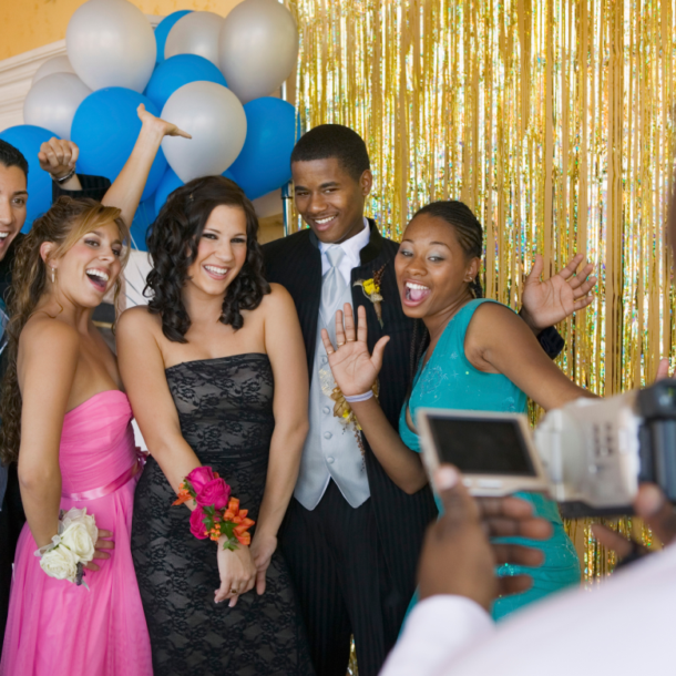 A group of four teenagers posing together with a gold backdrop at their high school prom