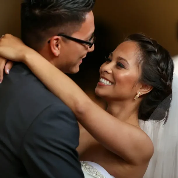 A newlywed couple smiling at each other, sharing their first dance together at their wedding reception